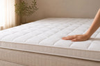 Verkoelende topper Elea Cool van Wonello® op een boxspring, hand voelt het quilted oppervlak. In lichte beige slaapkamer