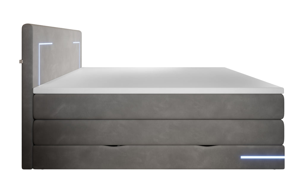 Zijaanzicht antraciet gestoffeerd bed met led-verlichting aan en op de topper een plaid en kussens. IN het onderste deel van het bed zijn 2 uitsparingen om de opbergruimte te openen.