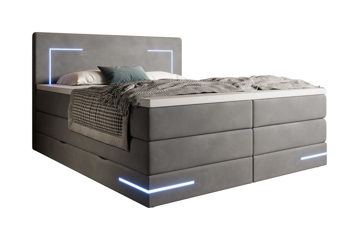 Diagonaal antraciet gestoffeerd bed met led-verlichting aan en op de topper een plaid en kussens.